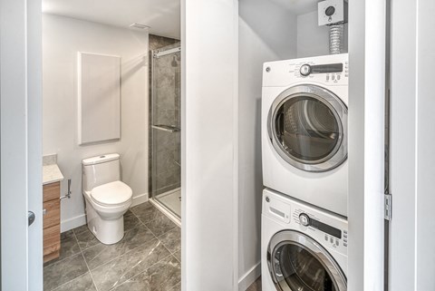A white toilet sits next to a washer and dryer in a small bathroom.