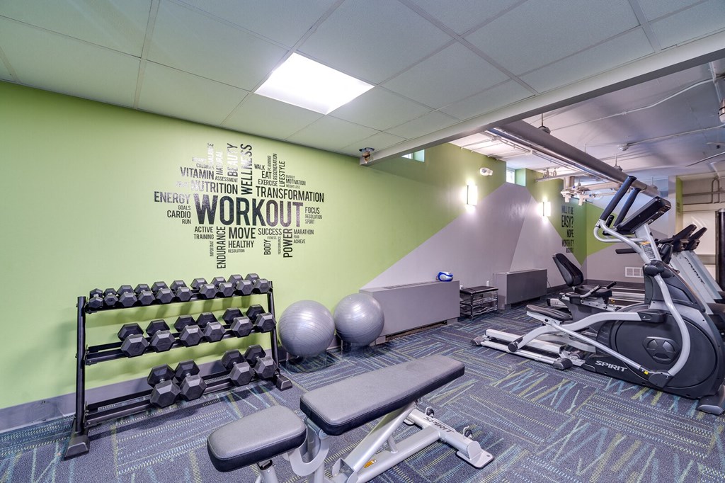 Resident gym with a green wall and a variety of exercise equipment such as an elliptical, weights, and exercise balls.
