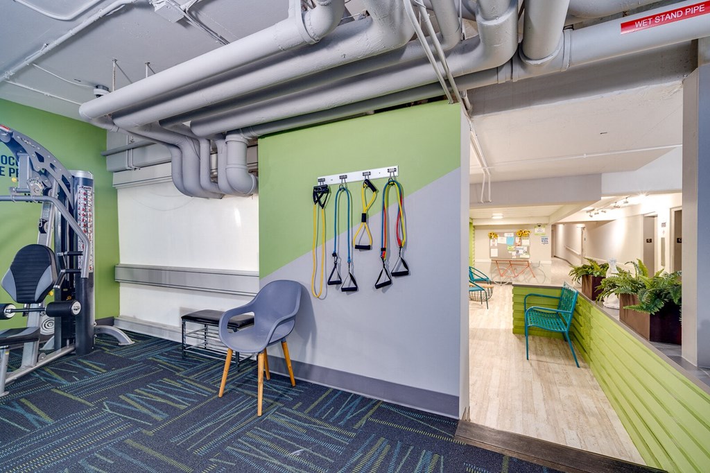 Resident gym with a green wall with resistance bands hanging on the wall, chair sitting against the wall, and weight machine at Dayton Towers apartments.