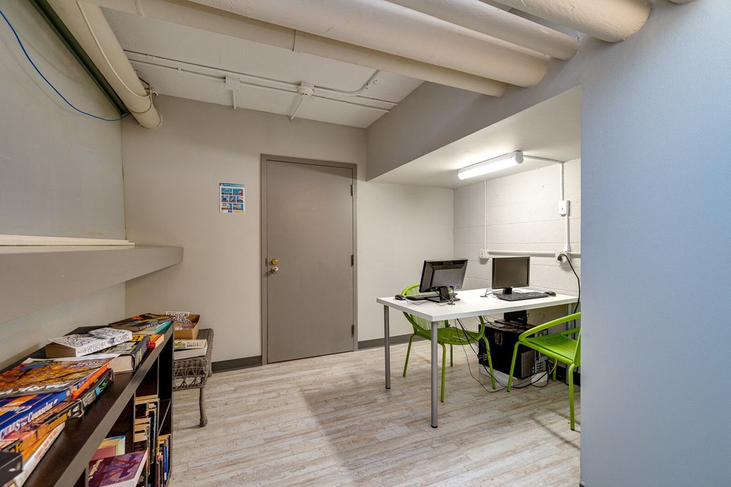 a room with a desk with a computer and a bookshelf