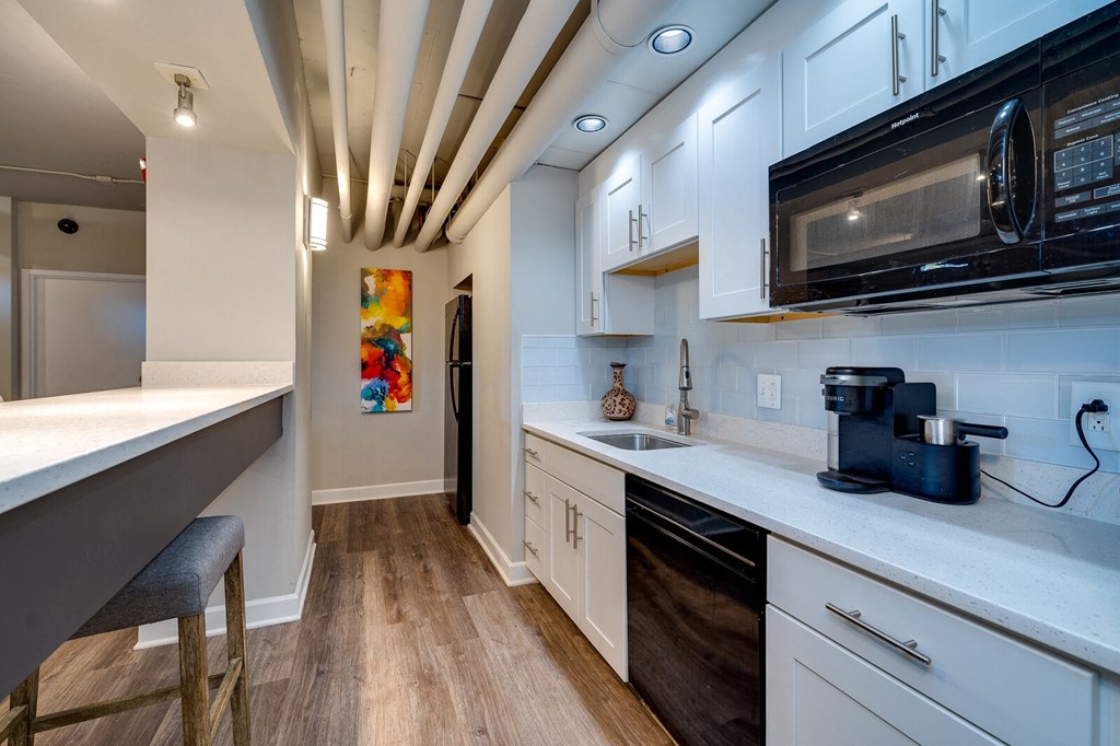 A kitchen with white cabinets, black appliances, breakfast bar, and hardwood-style flooring at Dayton, OH apartments