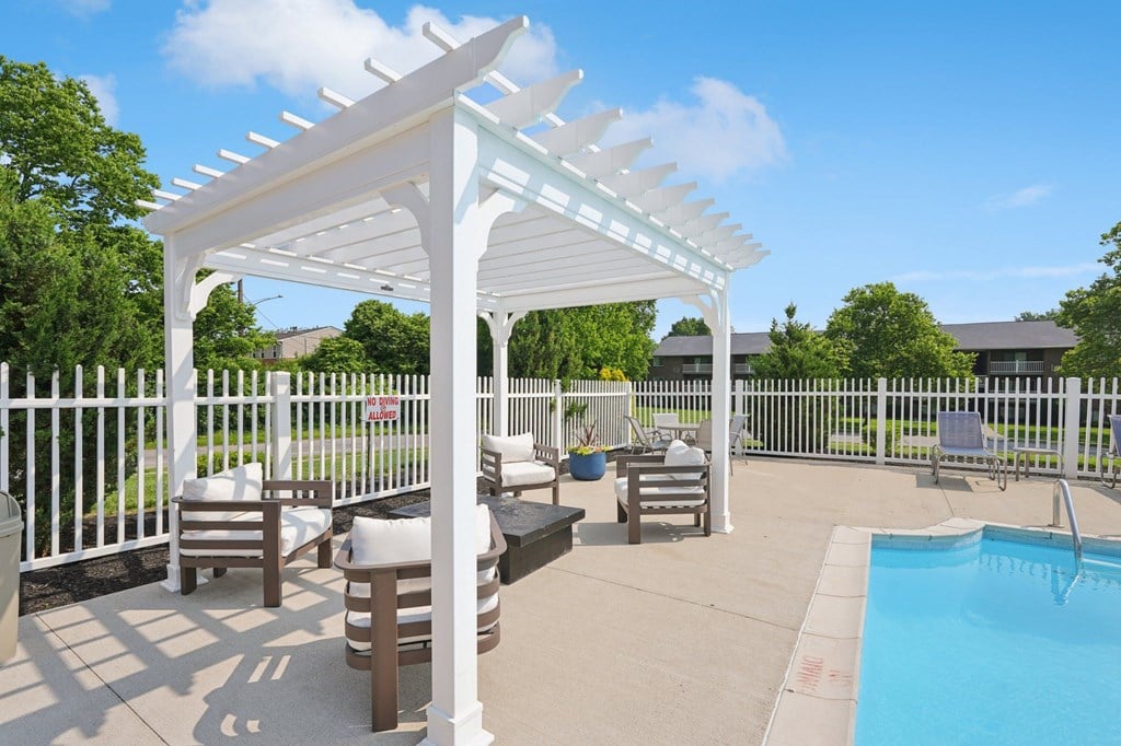 A white pergola is over a patio with a pool.