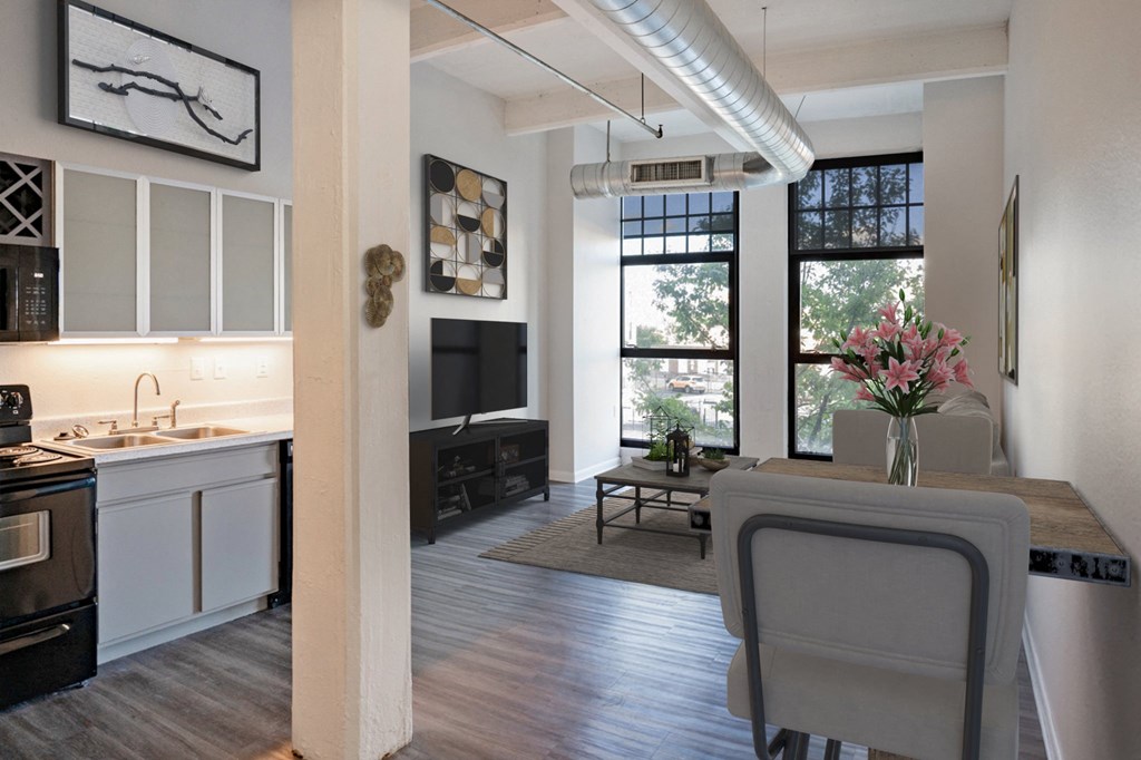 Open apartment space with hardwood style flooring, central air, and large windows allowing in natural lighting to the living area and kitchen