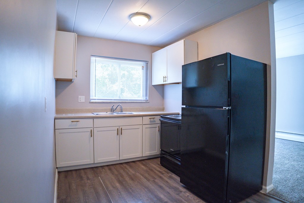 A black refrigerator in a kitchen with white cabinets.