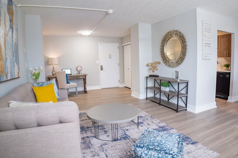 A living room with a grey couch, a white coffee table, and a round mirror on the wall.