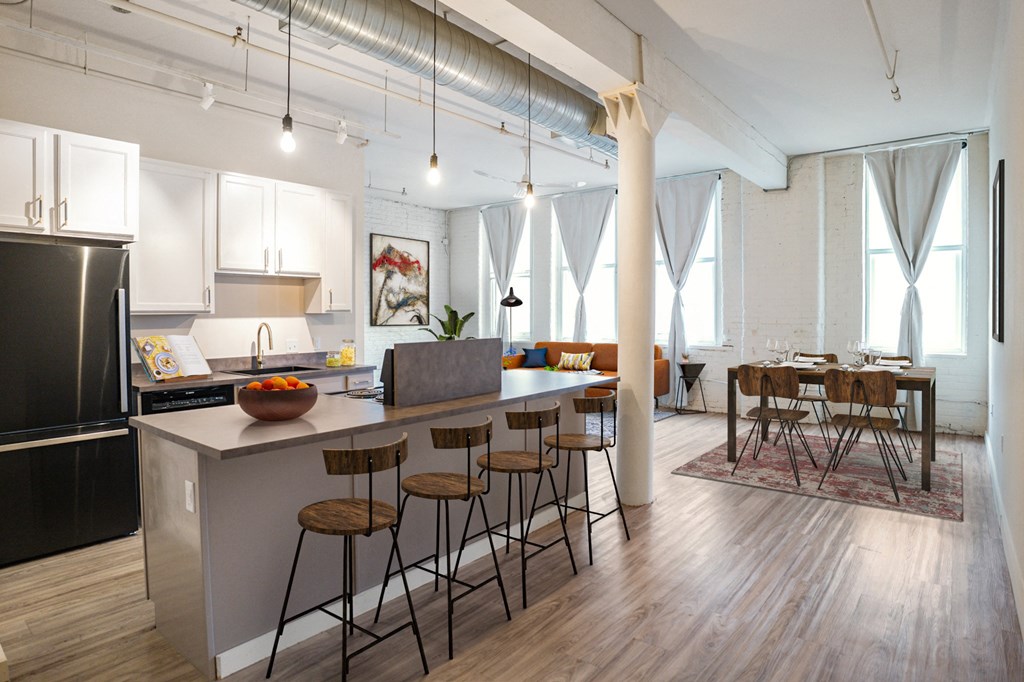 A kitchen with a black refrigerator, overhead lighting, lots of natural light, and wooden floors at The Cannery Lofts.