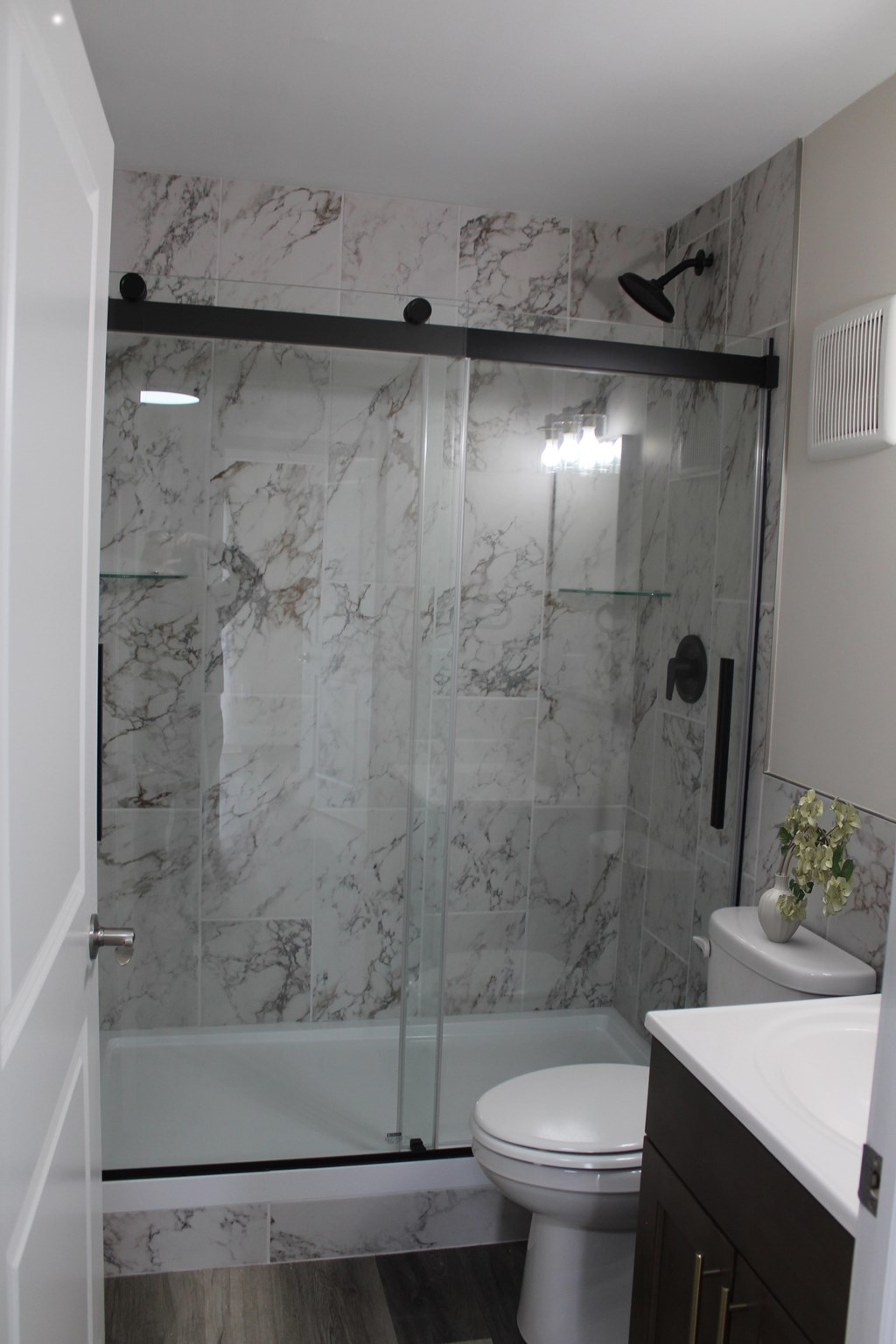 A white toilet sits in a marble bathroom next to a walk-in shower.
