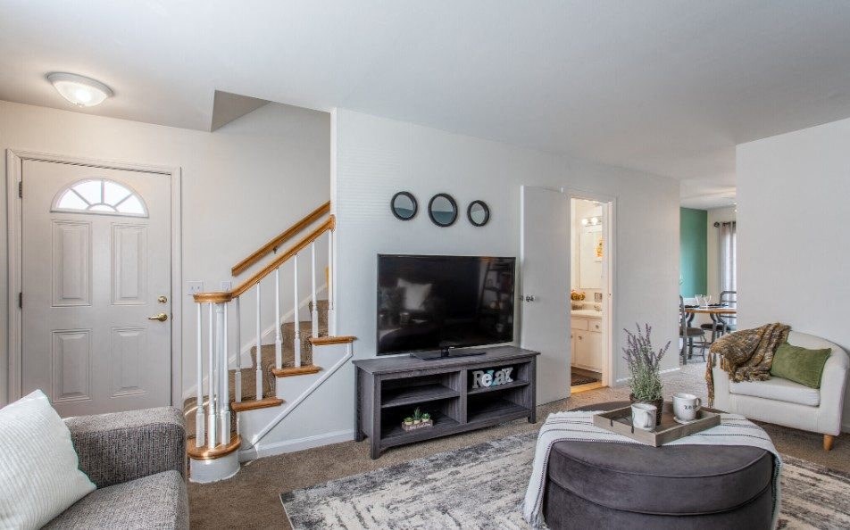 Model unit living room with a staircase in the background and a couch and chair in the foreground.