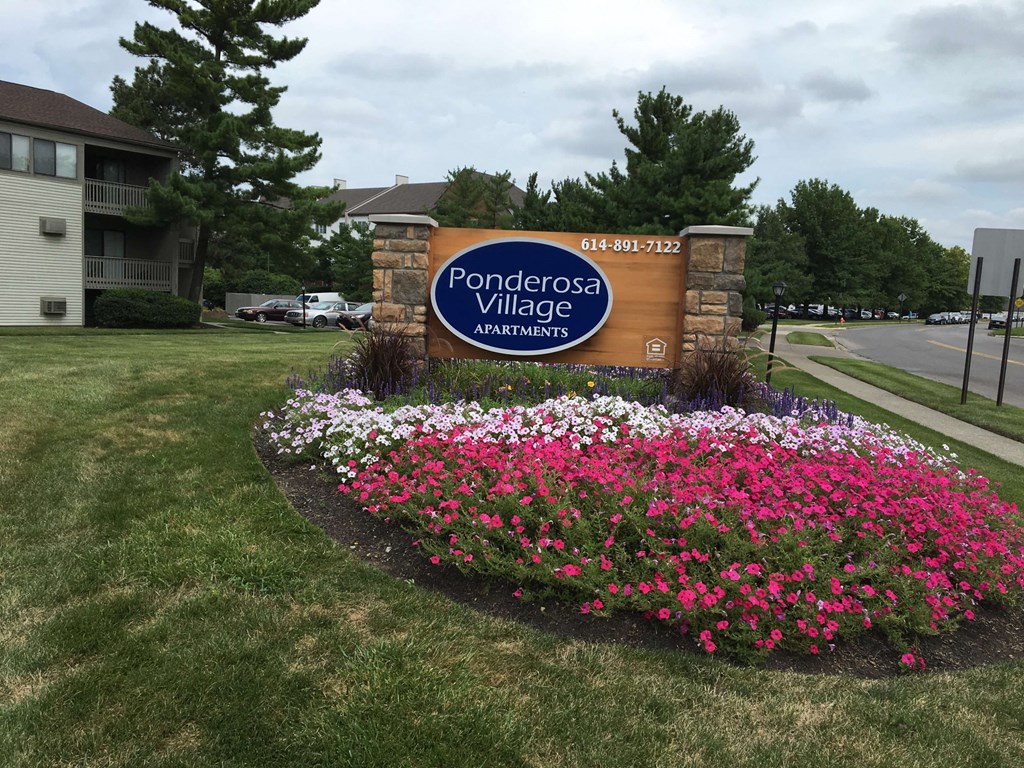a sign for the ponderosa village apartments on the grass with flowers