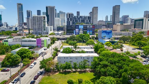 A cityscape with a mix of modern and older buildings, a road with cars, and a green park area.