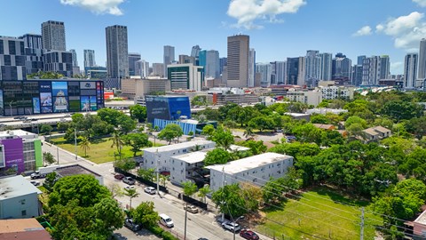 A cityscape with a mix of modern and older buildings, surrounded by greenery and a clear sky.