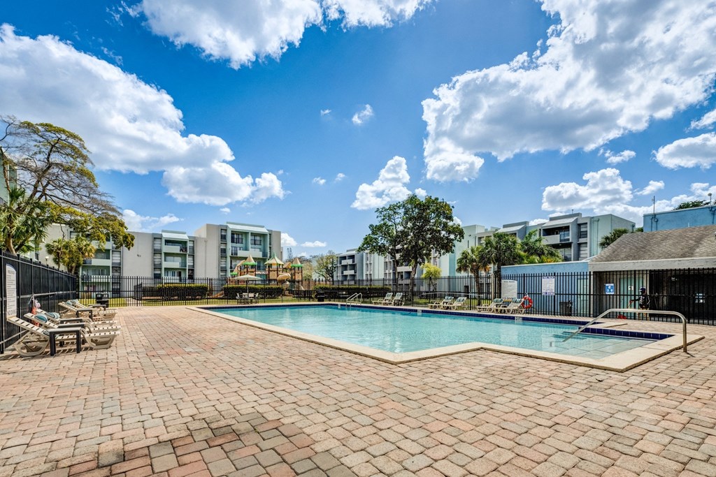 A swimming pool surrounded by a brick patio and buildings in the background.