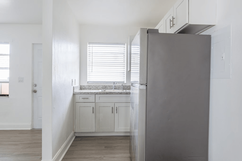 A kitchen with a refrigerator, cabinets, and a window with blinds.