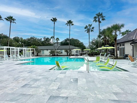 A pool area with a tiled floor and palm trees in the background.