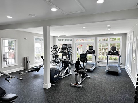A spacious gym with a variety of cardio equipment and a view of the outdoors through the windows.
