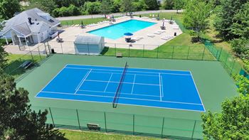A tennis court is surrounded by a pool and a house.