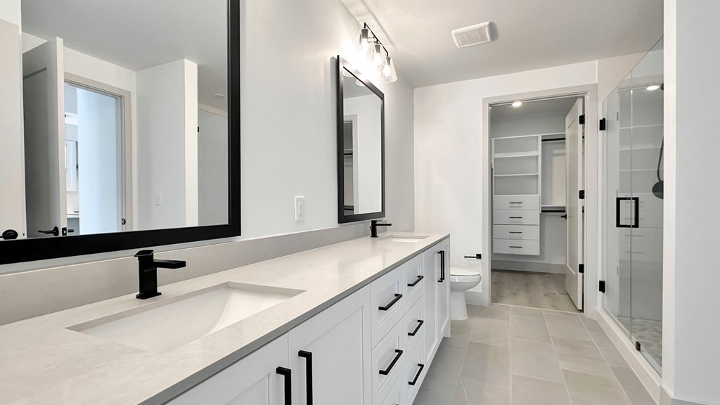 Spacious bathrooms with dual vanities, framed mirrors, quartz countertops and frameless walk-in showers