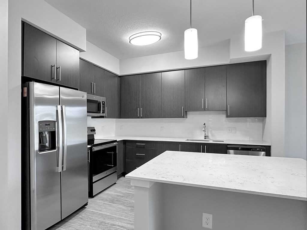 Fully-equipped kitchens with quartz countertops, large islands, tile backsplashes and stainless steel appliances
