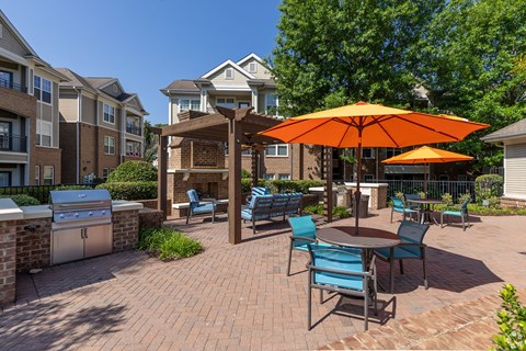 A patio with a table and chairs and an orange umbrella.