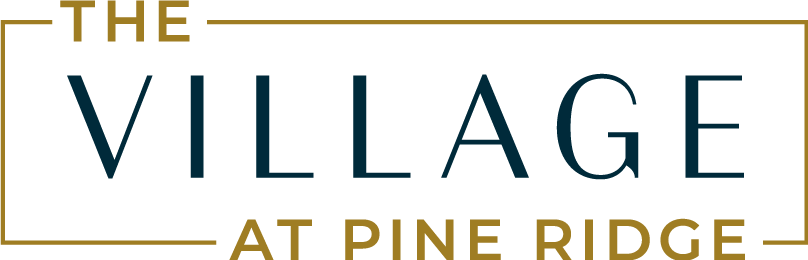 The image shows a sign with the text "The Village at Pine Ridge" in a stylized font.