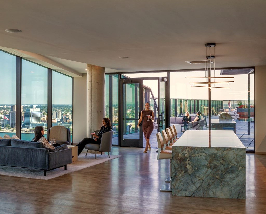 A woman in a brown dress is walking through a modern living room with a marble table and a view of the city.