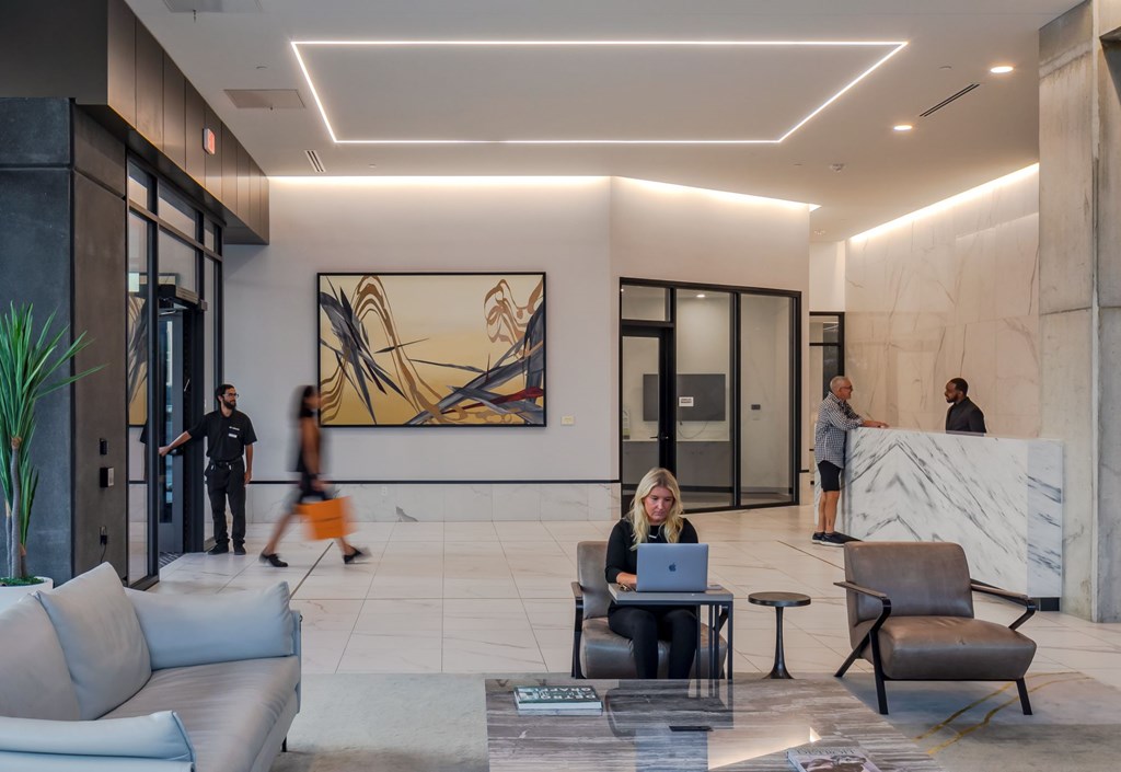 A woman is sitting at a table with a laptop in a modern lobby area.