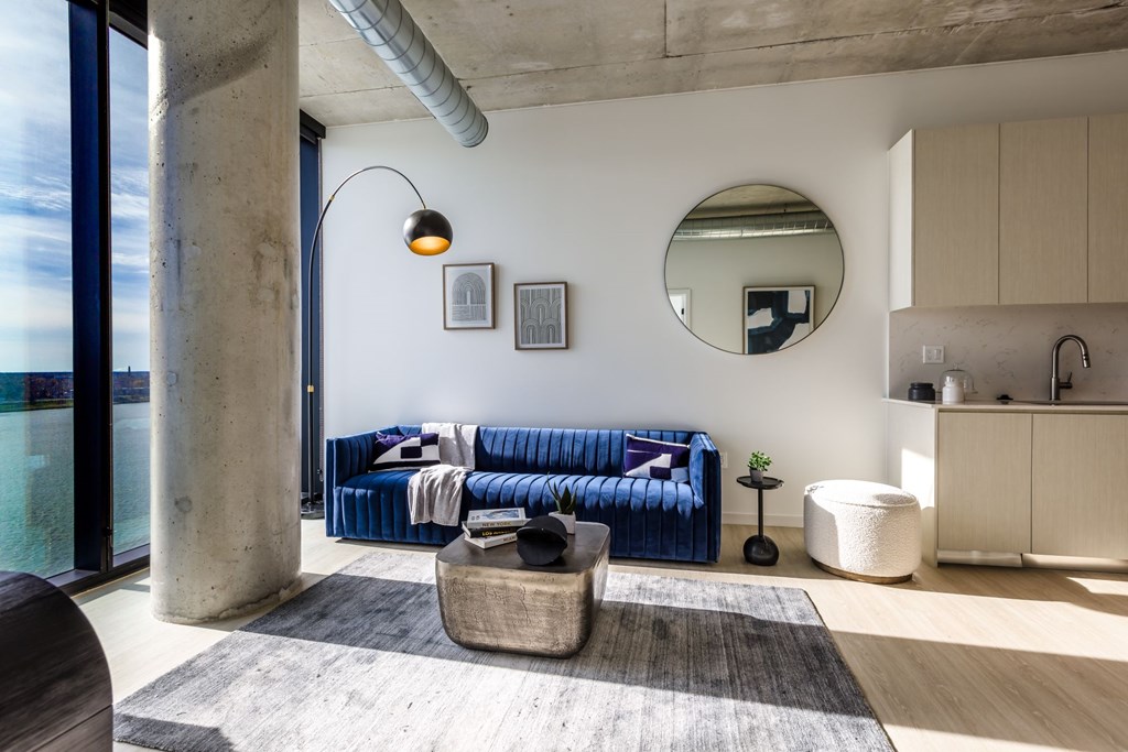 A blue sofa sits in a modern living room with a round mirror and a concrete pillar.