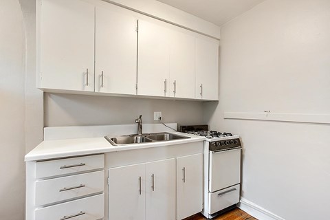 A white kitchen with a sink, stove, and cabinets.