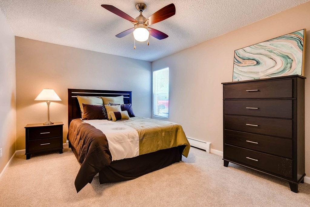 A bedroom with a bed, dresser, and ceiling fan.