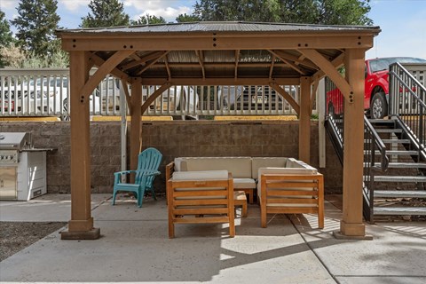 A wooden gazebo with a couch and chairs is in the foreground with a red car and stairs in the background.