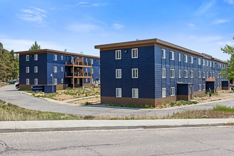 A blue building with a brown roof is surrounded by a grassy area and a paved road.