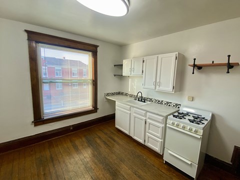 A kitchen with a white stove top oven and white cabinets.