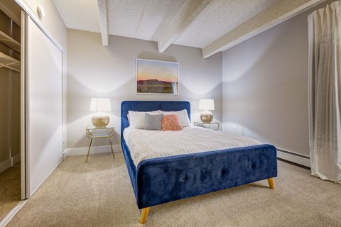 A bedroom with a blue bed and a painting on the wall.