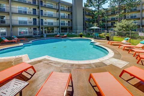 A round swimming pool surrounded by orange sun loungers.