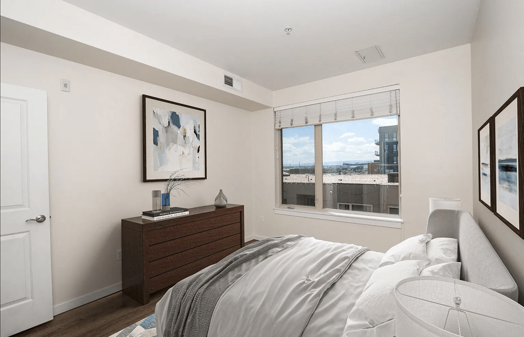 A bedroom with a bed, nightstand, and a window overlooking a cityscape.