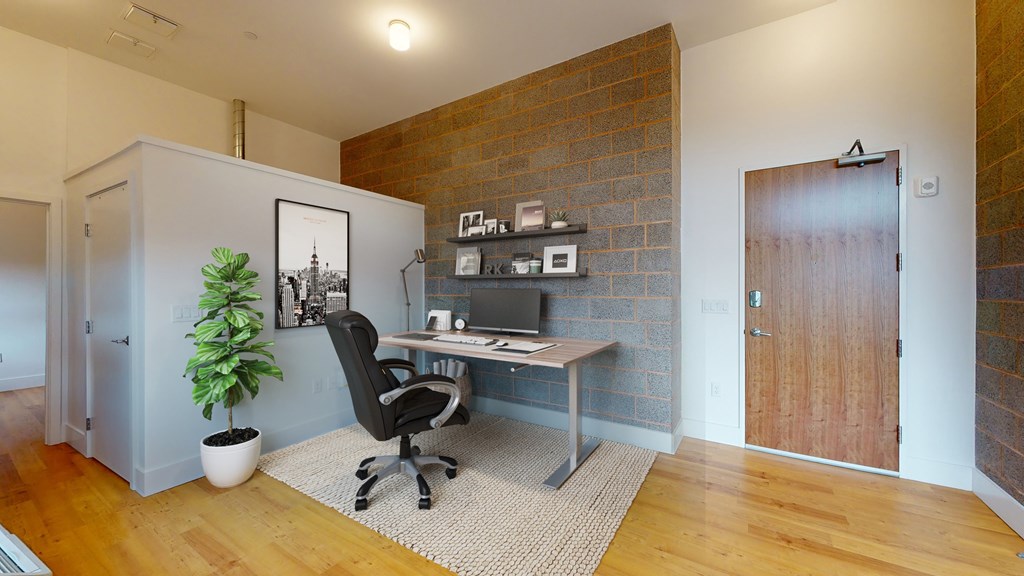 A room with a desk and a chair in front of a brick wall.