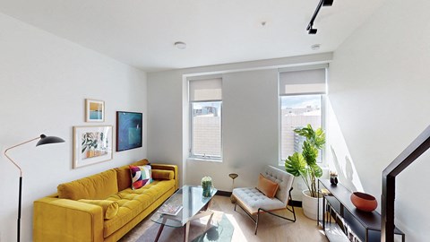 A living room with a yellow couch and a glass table.