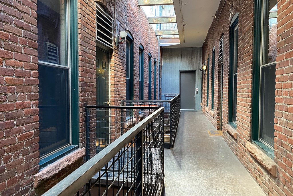 Partially covered  long exterior hallway with brick walls and a metal railing.