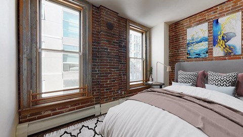A bedroom with a large bed and an exposed brick wall with 2 large floor-to-ceiling windows.