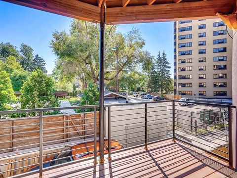A balcony with a table and chairs overlooks a parking lot and buildings.