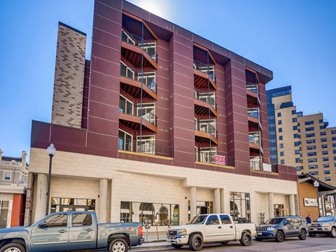 A modern building with a red facade and a parking lot in front.
