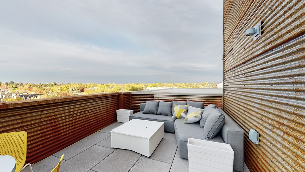 A patio with a white couch and yellow chairs overlooking a field.