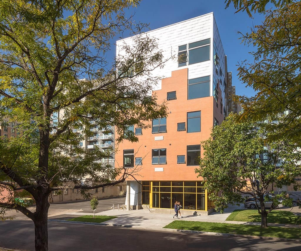 A modern building with orange and white panels is surrounded by trees.