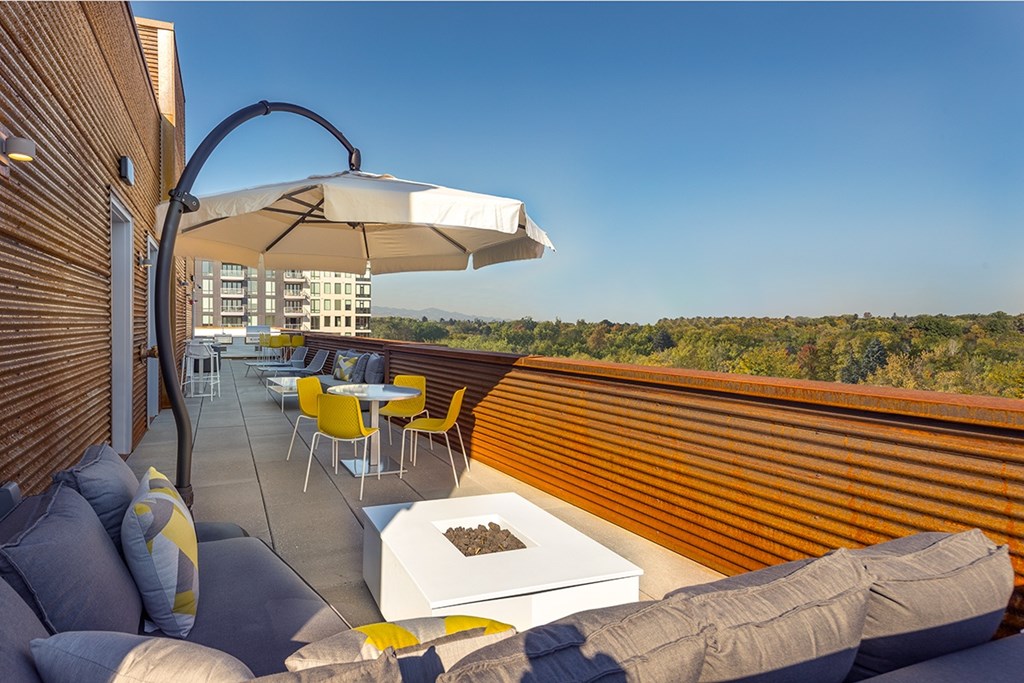 A patio with a white umbrella and a grey couch.