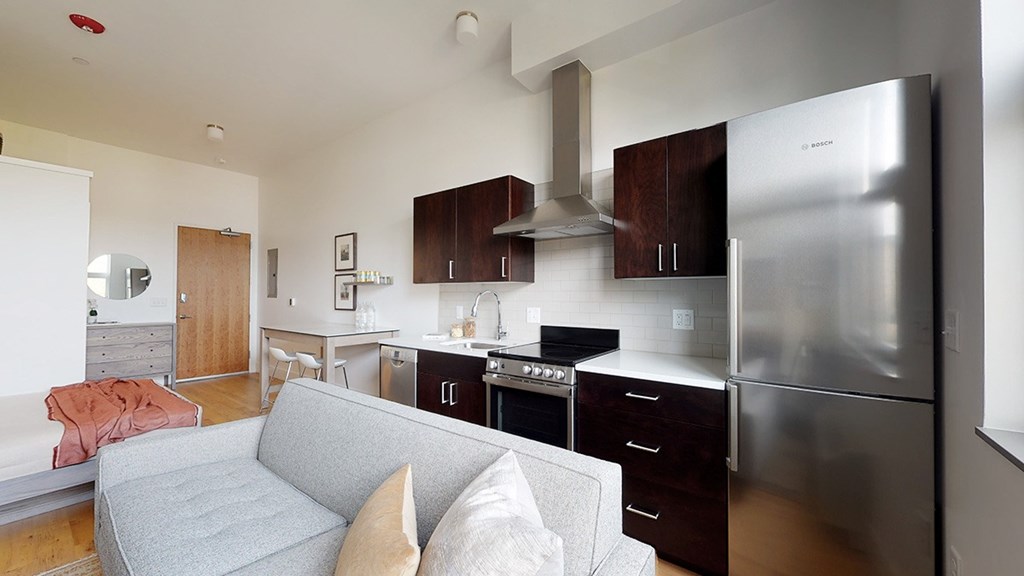 A modern kitchen with a grey couch and a stainless steel refrigerator.