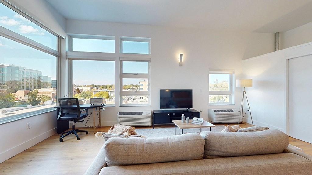 A living room with a couch, a television, and a window overlooking a cityscape.