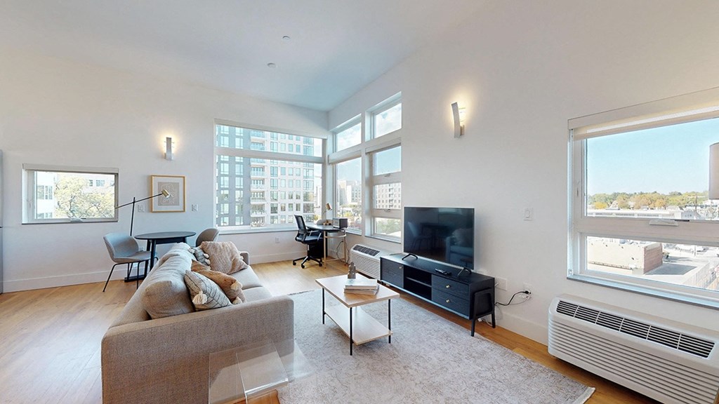 A living room with a grey couch, a white coffee table, a black television, and a large window with a view of the city.