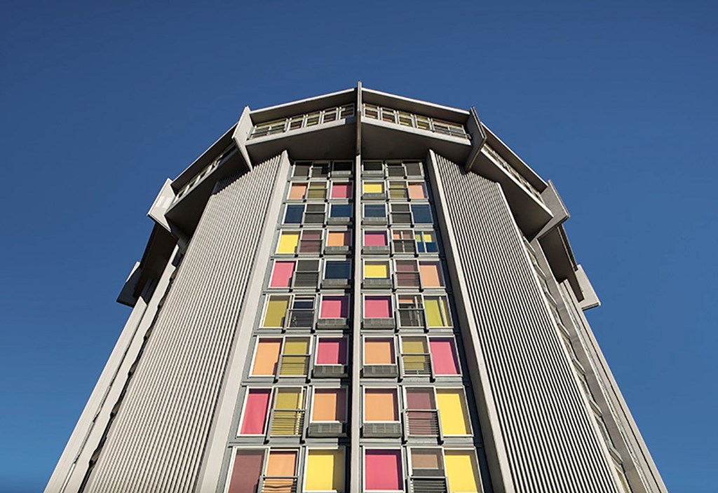A tall building with a row of windows in red, yellow, orange, and pink.