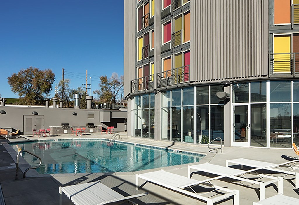 A swimming pool is surrounded by sun loungers in front of a modern building.