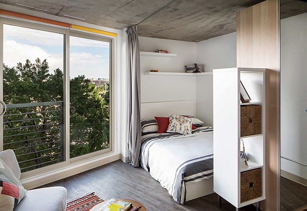 A bedroom with a bed, a chair, and a window with a view of trees.